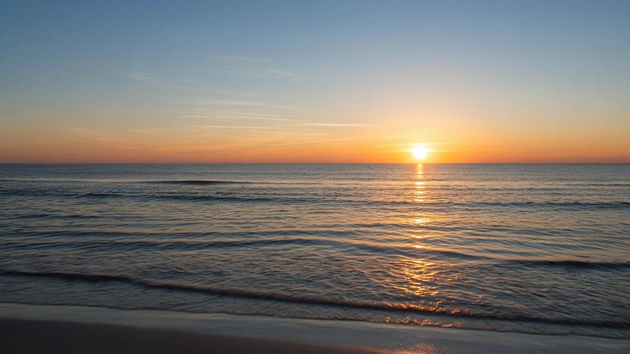 The sun rising over a calm ocean, with a gold path of light across the water.
